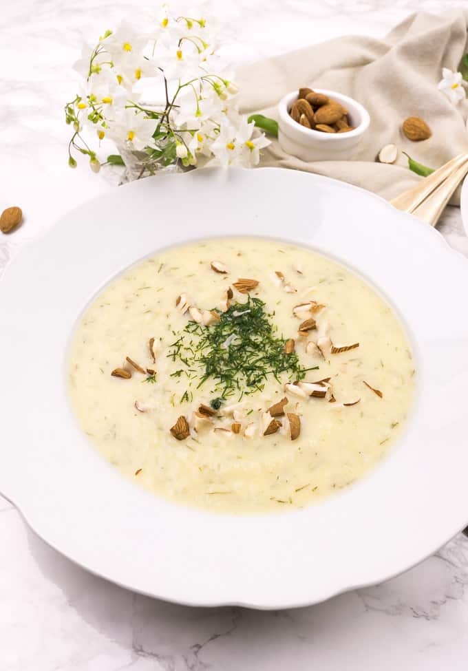 Creamy celeriac soup on a plate, topped with chopped almonds and dill