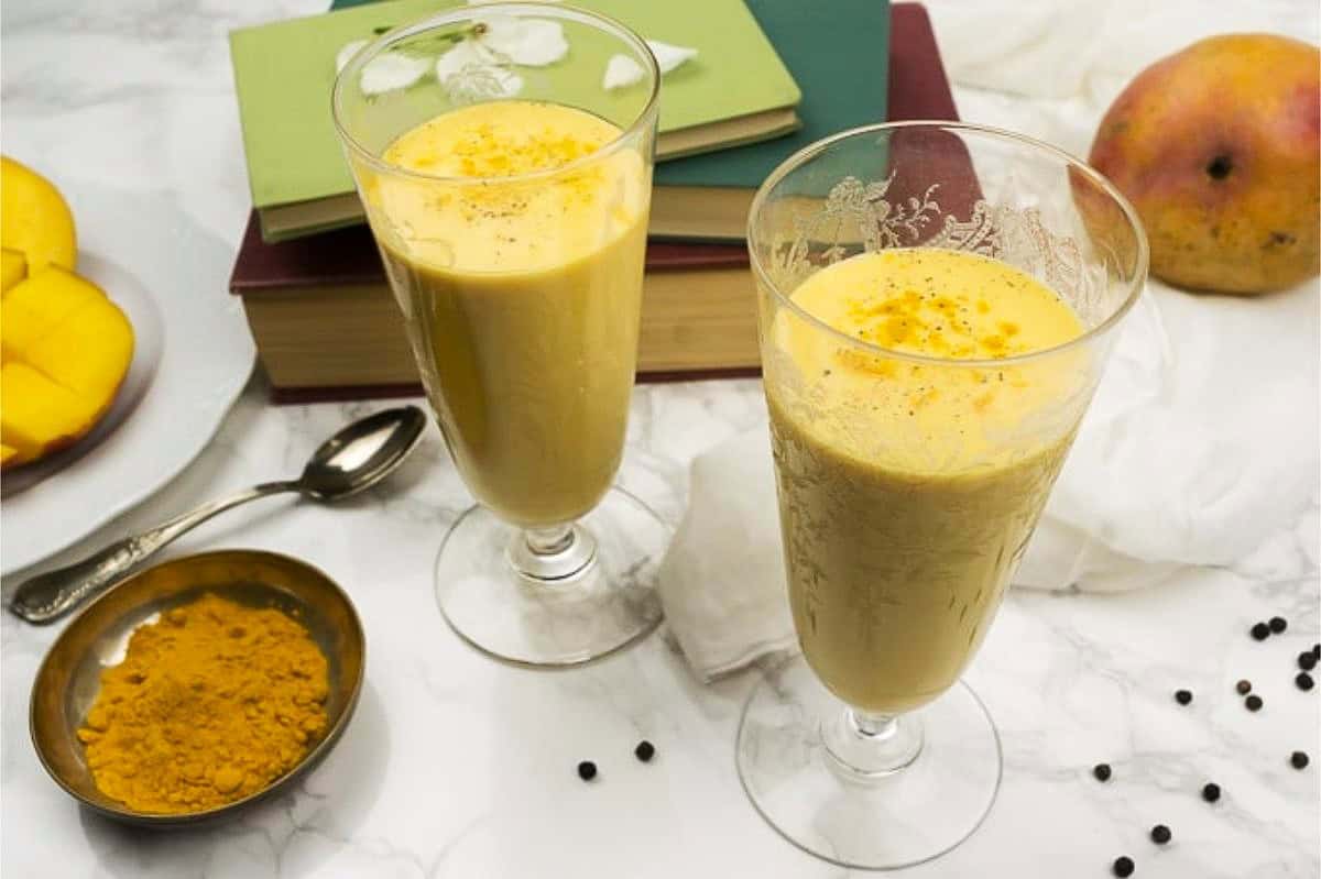 two mango lassi glasses next to ground turmeric