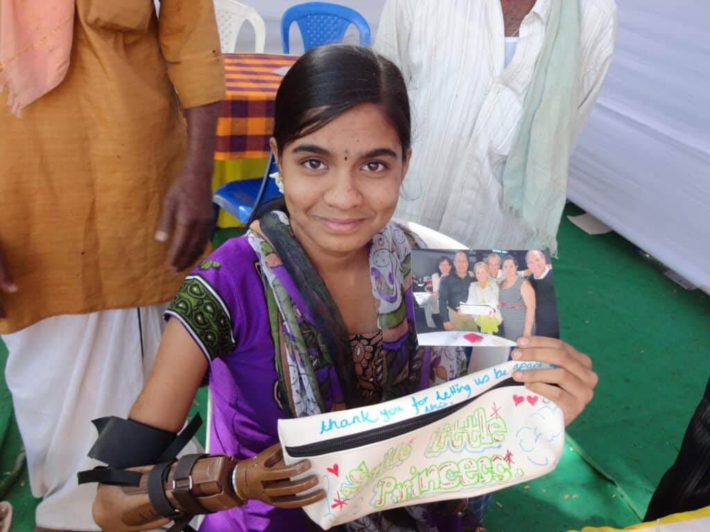 A smiling girl with her prosthetic hand presenting the picture of the team who assembled her prosthetic hand in a team-building activity