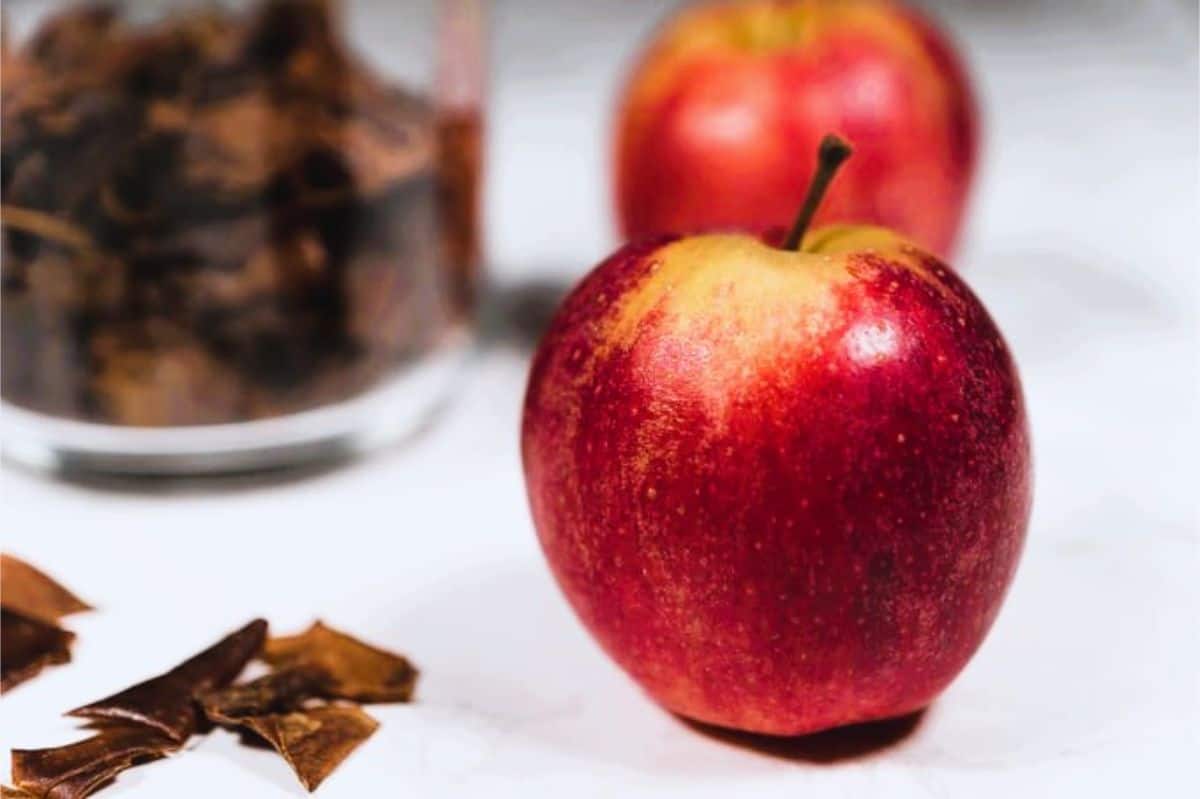 Crispy apple skins made from dried apple peels stored in a glass jar, with fresh red apples in the background