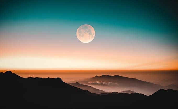 Peach-colored moon over dark mountains