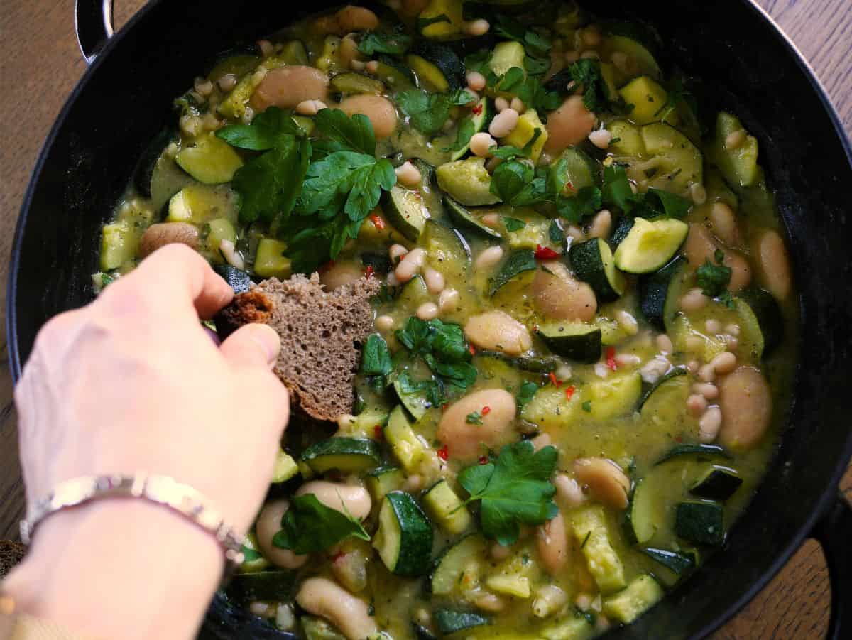 dipping bread into the pan of stewed zucchini with beans